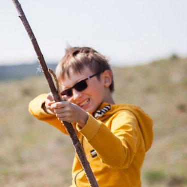 A happy child in sunglasses playing with a stick outdoors, capturing the essence of fun and energy.