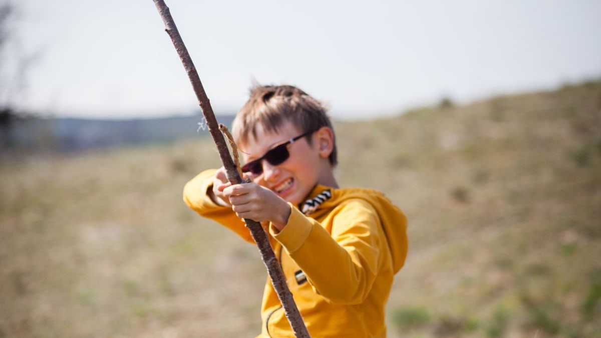 A happy child in sunglasses playing with a stick outdoors, capturing the essence of fun and energy.